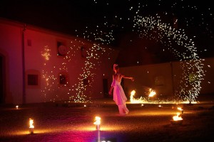 Feuertänzerin in weissem Kleid umgeben von Funkenregen bei Feuershow für Hochzeit