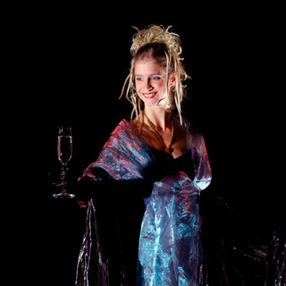 Blonde Stelzenläufein in blauem Abendkleid mit Sektglas